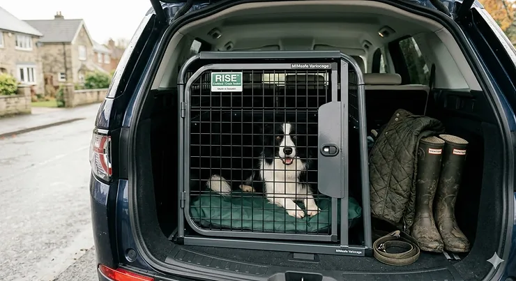 A heavy-duty crash tested dog crate securely installed in the boot of a Land Rover, showing the emergency escape hatch and reinforced frame. crash tested dog crate
