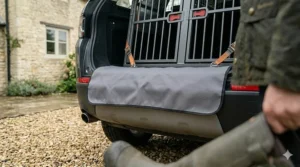 A grey fabric bumper protector mat draped over a car's rear bumper to prevent scratches when loading a double dog crate.